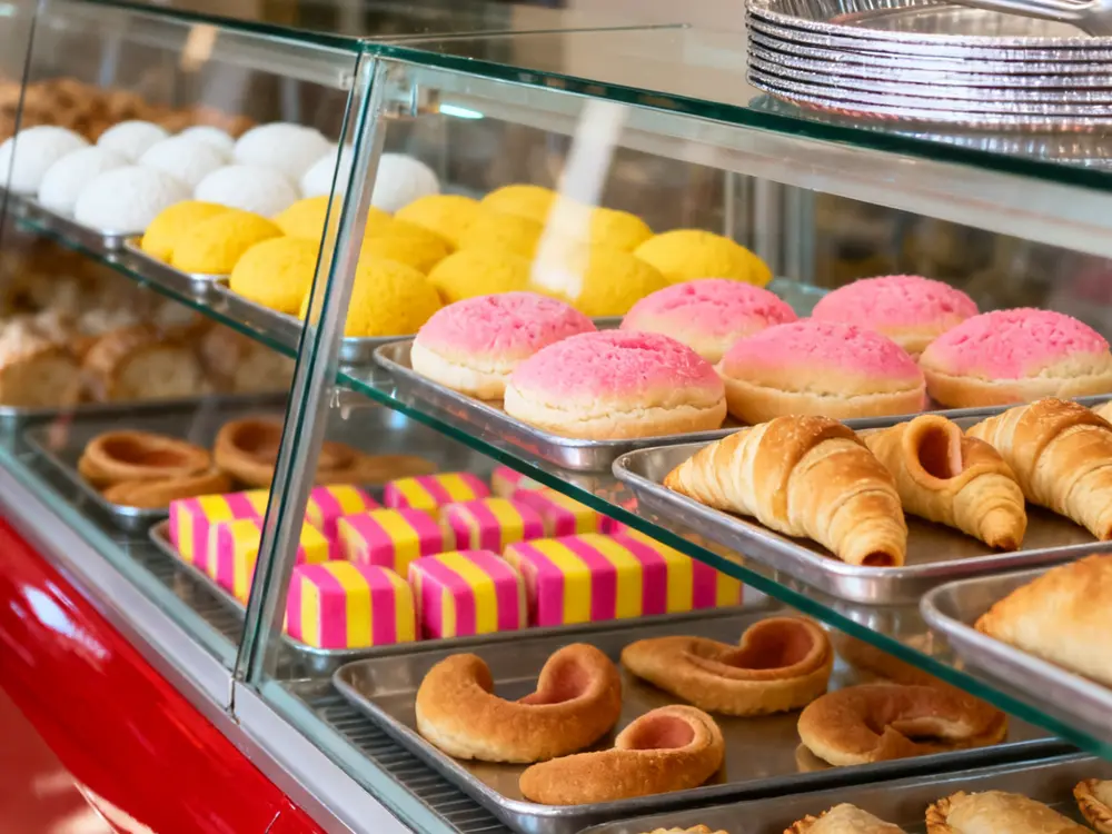 Trays of white, yellow and pink conchas and cuernos inside the display case